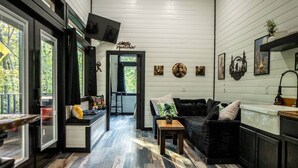 A cozy interior with a black sofa, a small table, and a TV mounted on the wall. - Sasquatch soak shack (Mena)