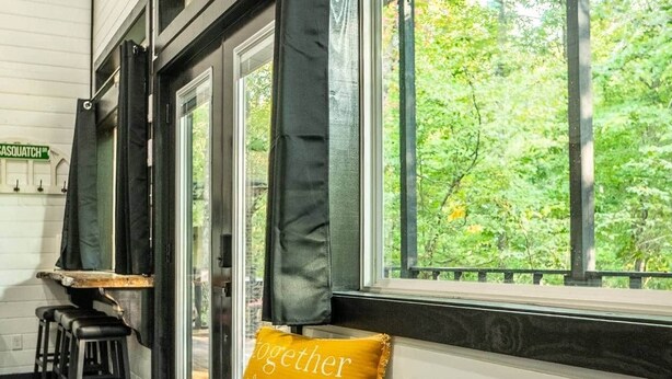 A cozy seating area with a bench, a window with a view of trees, and a sign reading 'CASQUATCH'. - Sasquatch soak shack (Mena)