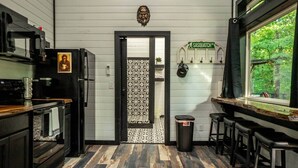 A kitchen with a patterned door, a window with a view of greenery, and a sign reading 'SASQUATCH DR.' - Sasquatch soak shack (Mena)