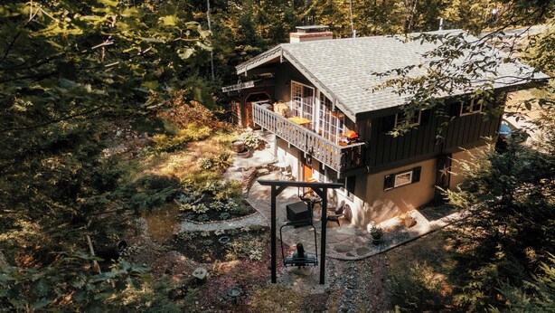 Une cabane dotée d’un balcon, entourée d’une forêt dense.