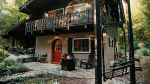 Une cabane en rondins à deux étages, dotée d’un balcon, d’une terrasse en pierre et d’un espace salon extérieur.