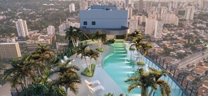 A high-rise building with a rooftop pool surrounded by palm trees and lounge chairs. - Brand New Apartment | AirBrooklin (São Paulo)