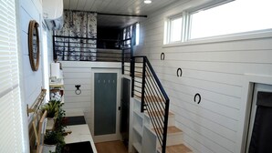 Una escala amb baranes negres que condueix a un segon pis, parets amb panells blancs i una porta amb vidre acidificat.