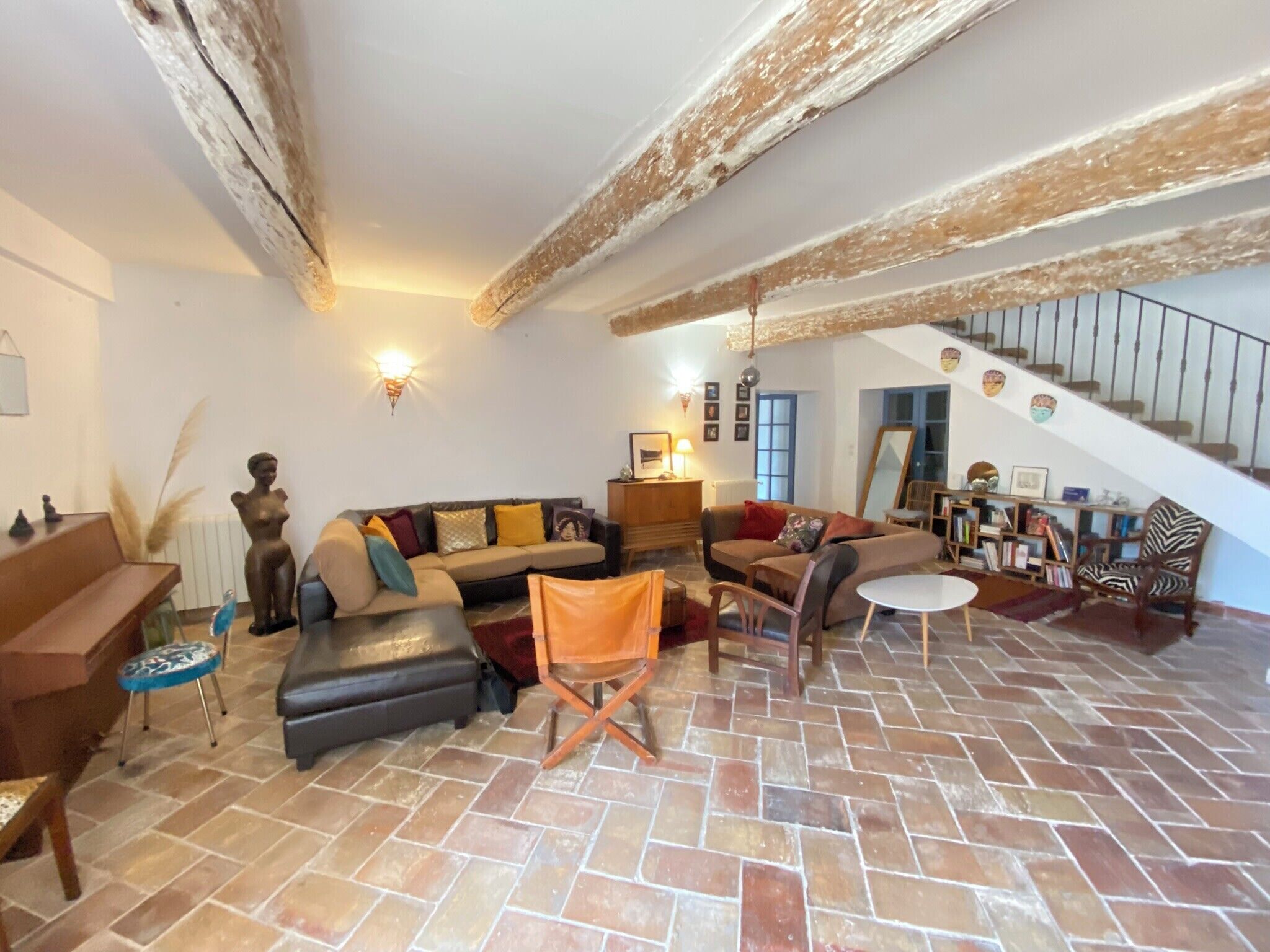 A spacious living room with a large sectional sofa, a small table, and a chair. There is a staircase leading to an upper level.