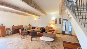 Un salón acogedor con suelo de piedra, un conjunto de sofás, una mesa de centro de madera y una escalera con barandilla de metal.