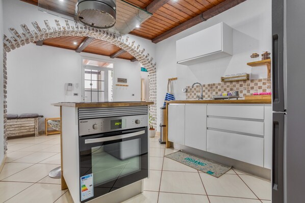 Una cocina con horno empotrado, armarios blancos, encimera de madera y suelo de baldosas.