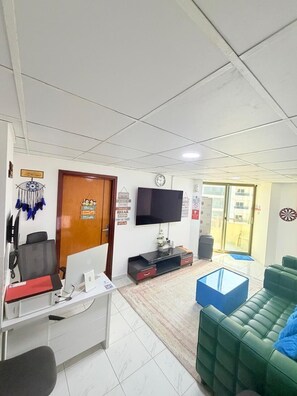 Un espace d’accueil comprenant un bureau, des chaises, un téléviseur et un canapé vert.
