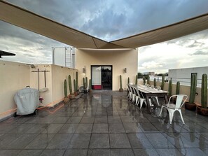 Une terrasse sur le toit, avec une table et des chaises, des cactus en pot et un barbecue couvert.