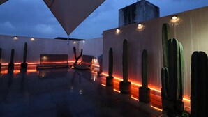 Eine Außen-Terrasse mit spiegelndem Boden, einem großen Sonnenschirm und Kakteen an den Wänden.