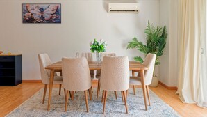 Comedor con mesa de madera y seis sillas, un florero con flores y una planta grande en maceta.