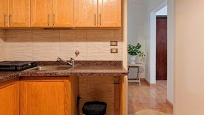 Una cocina con armarios de madera, encimera de granito, pileta de acero inoxidable y un cesto de basura pequeño.