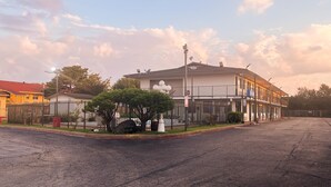 A two-story building with a gated entrance, a parking lot, and a clear sky. - Motel 6 Dallas, Tx – St. Augustine / Hwy 175 (Dallas)