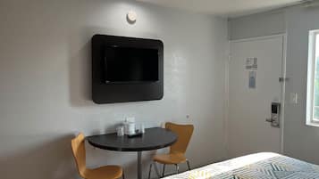 Een hotelkamer met een flatscreen televisie aan de muur, een klein rond tafeltje met twee stoelen, en een deur met een raam.