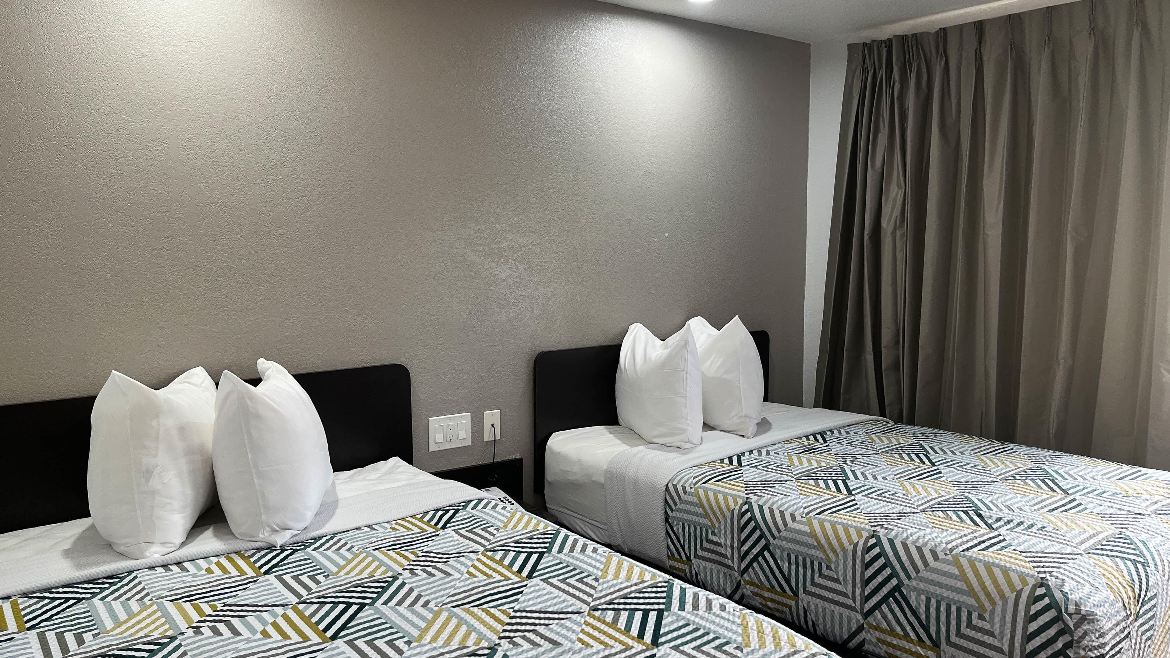 A hotel room with two beds, each with patterned bedding and white pillows.
