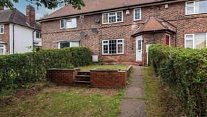A two-story brick house with a red door, satellite dishes, and a small garden with a brick wall and steps leading to a door.