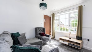 A modern living room with a grey sofa, a grey armchair, a wooden side table, and a large window with curtains.