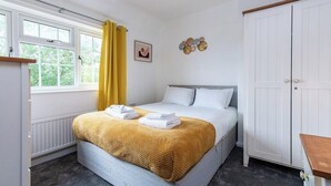 A bedroom with a bed, a window with yellow curtains, a radiator, and a wardrobe.