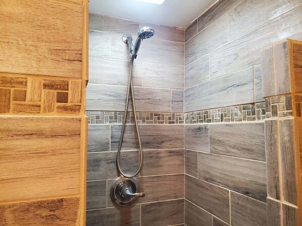 A shower with a handheld showerhead and a wall-mounted faucet, set in a corner with wooden and tiled walls.
