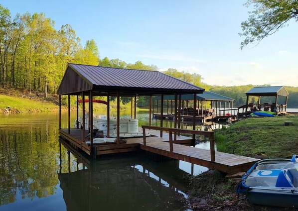 A lakeside dock with a covered seating area and a boat.