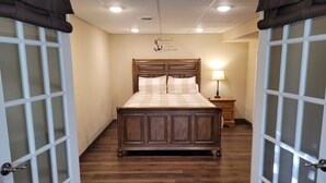 Un dormitorio con una cama de madera, una mesita de noche con lámpara y una pared con un letrero decorativo.