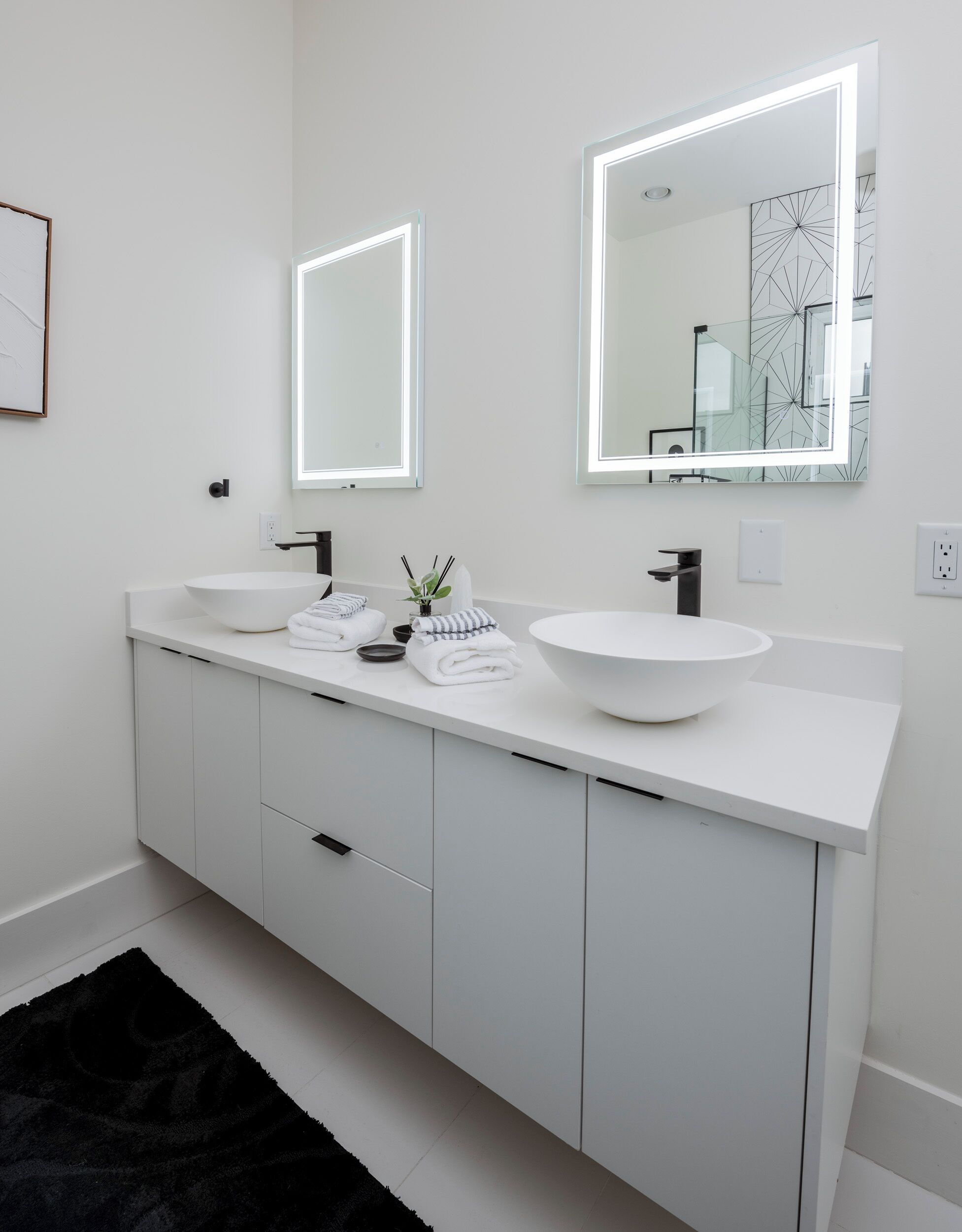 Un bagno moderno con due grandi specchi, un mobile lavabo bianco e un tappeto nero.