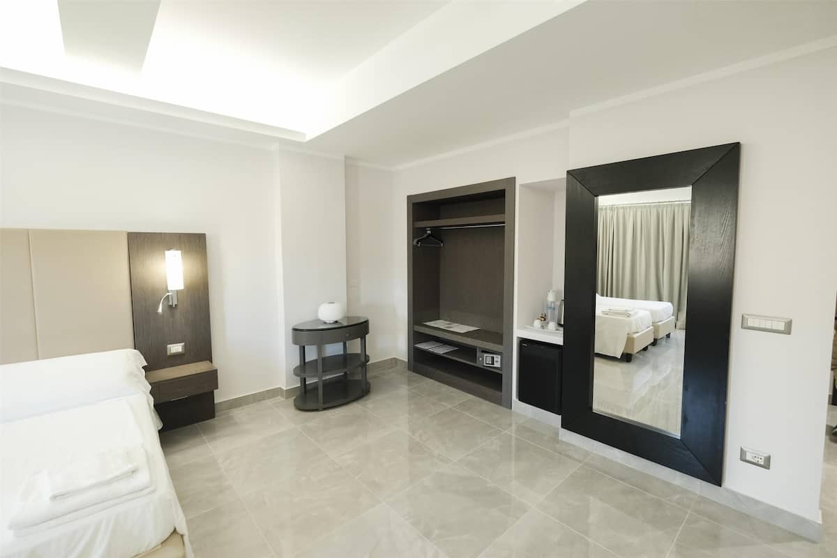A modern hotel room with a bed, a bedside table, a mirror, a wardrobe, and a small round table.