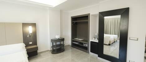 Una habitación de hotel moderna con cama, mesita de noche, espejo, armario y una pequeña mesa redonda.