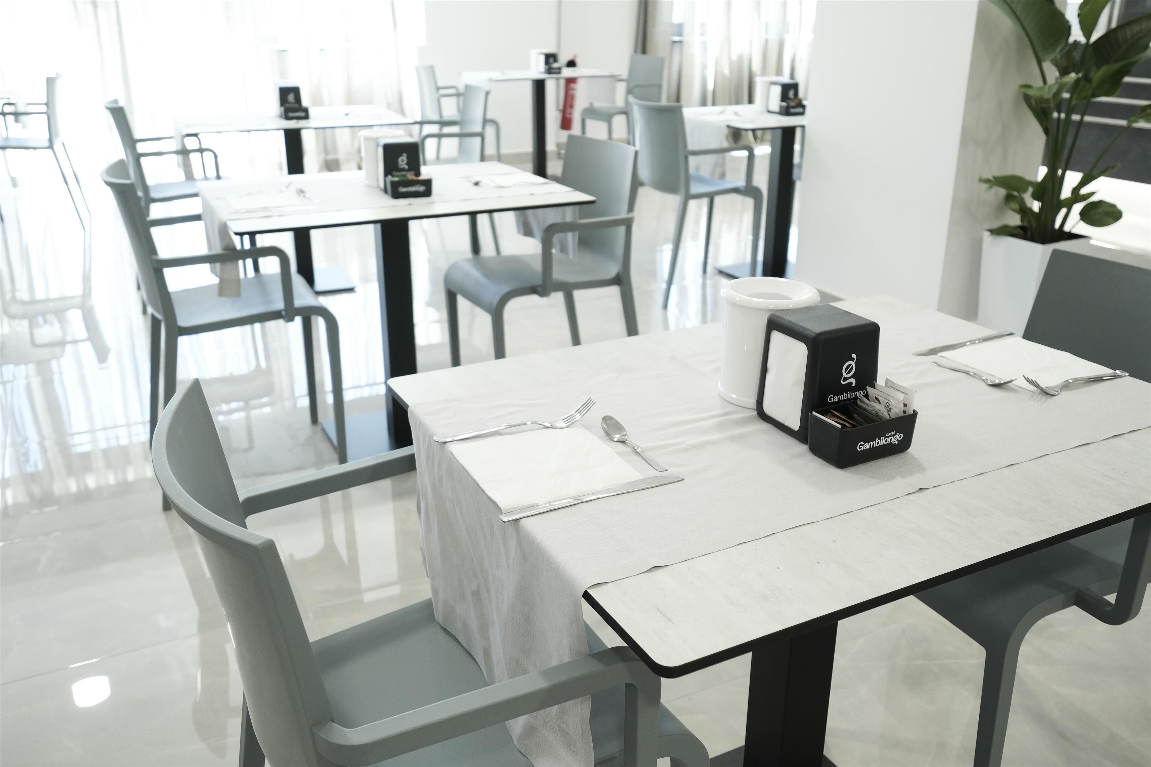 A modern dining area with tables set for two, featuring a white tablecloth, cutlery, and a black box with the text 'Gambilong'.