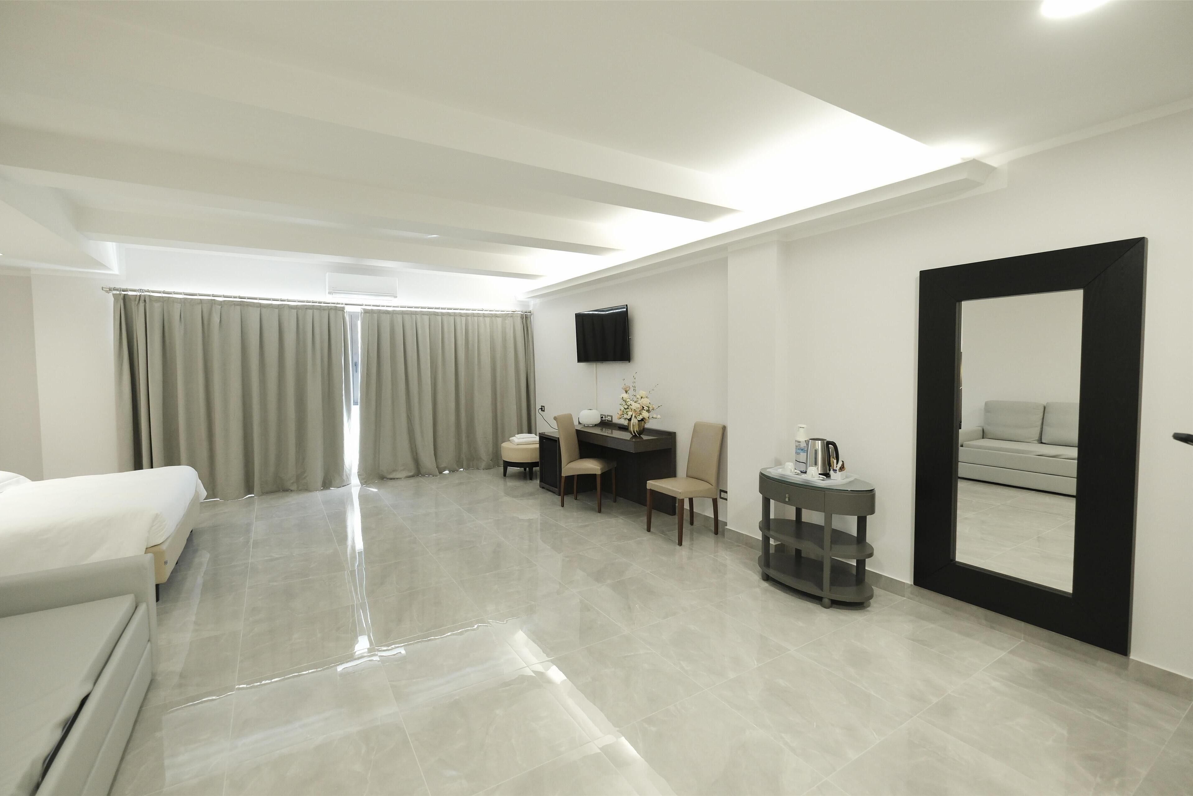 Habitación de hotel con cama, escritorio, sillas, televisor y un espejo grande.