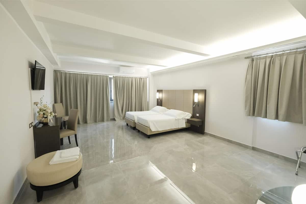 A modern hotel room with a large bed, a desk, a chair, a small sofa, and a TV mounted on the wall.