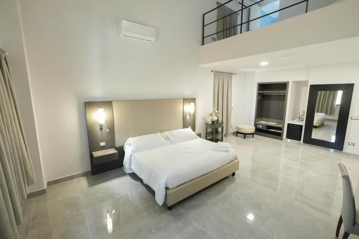 A modern hotel room with a large bed, a built-in vanity with a mirror, a small seating area, and a walk-in closet.