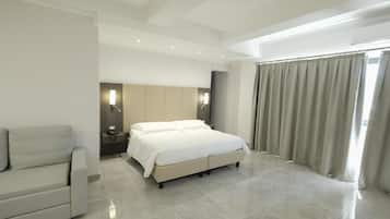 A modern hotel room with a large bed, a sofa, a bedside table, and a mirror.