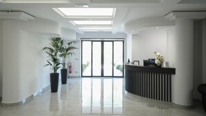 A modern reception area with a black reception desk, potted plants, and a glass door leading outside.