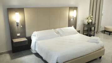A hotel room with a large bed, bedside tables, a nightstand, a small table with a vase of flowers, and a curtain.