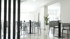 A modern hotel lobby with a reception desk, several chairs, a large potted plant, and a glass partition.
