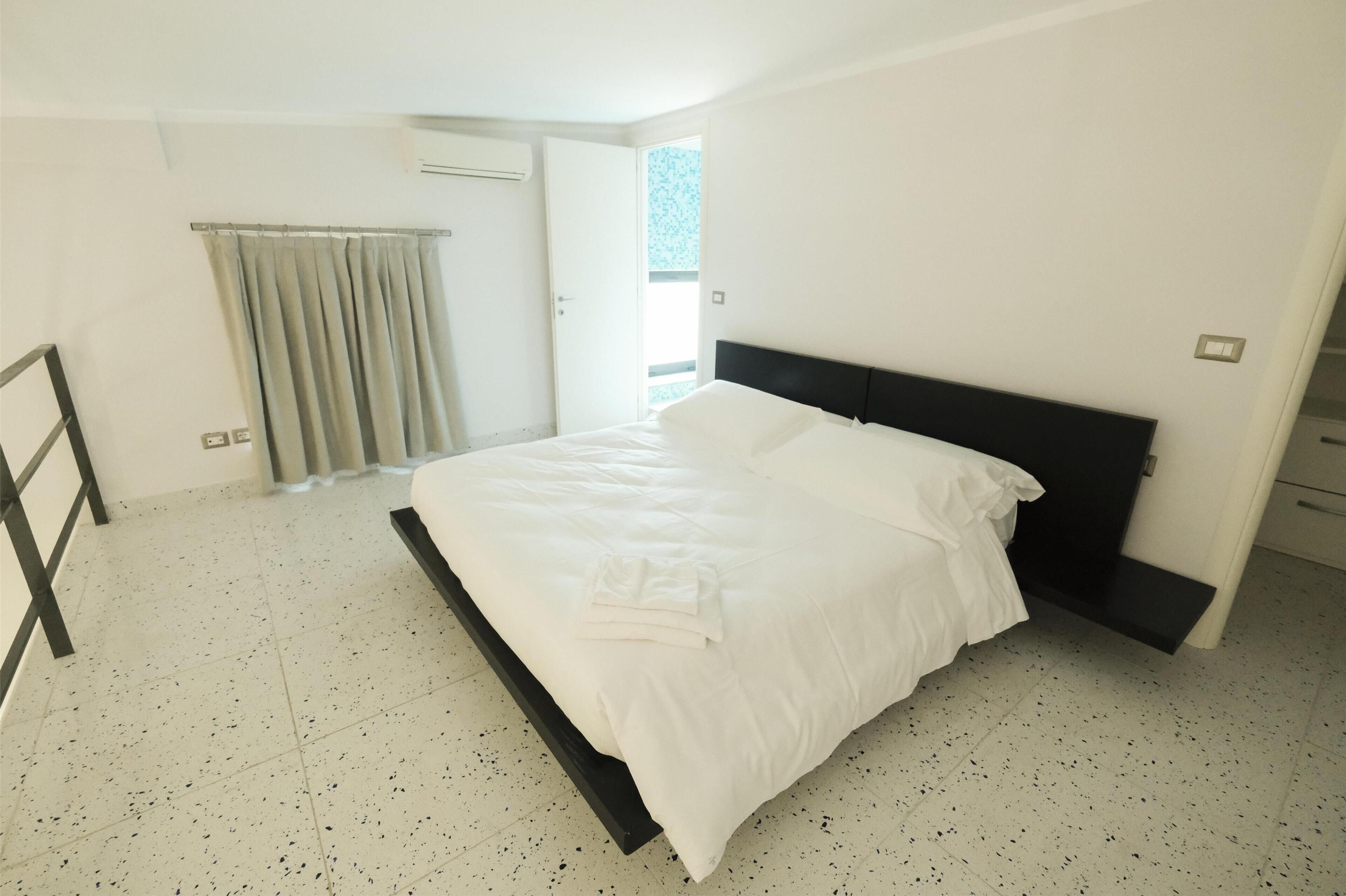 Un dormitorio con una cama, una ventana con cortinas y una puerta.