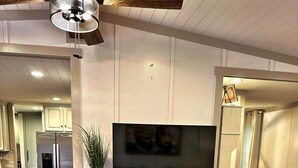 A modern living room with a wooden entertainment center, a flat-screen TV, and a dining area with a wooden table and chairs. - Lakefront Retreat + Dock + Kayaks + Fire Pit + Lakefront Kitchen (Milledgeville)