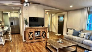 A modern living room with a wooden coffee table, a grey sofa, and a TV on a wooden cabinet. - Lakefront Retreat + Dock + Kayaks + Fire Pit + Lakefront Kitchen (Milledgeville)