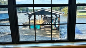 A view of a dock with a covered structure, a boat, and a building in the background. - Lakefront Retreat + Dock + Kayaks + Fire Pit + Lakefront Kitchen (Milledgeville)