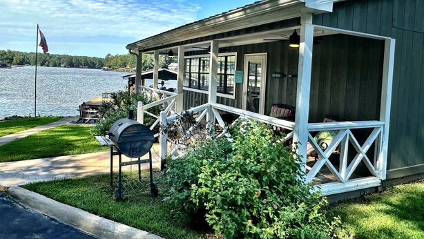 A lakeside cabin with a covered porch, a grill, and a flag. - Lakefront Retreat + Dock + Kayaks + Fire Pit + Lakefront Kitchen (Milledgeville)