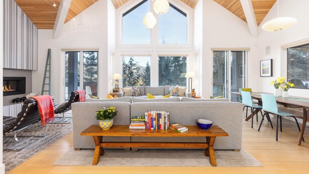 Een ruime woonkamer met een grote hoekbank, een houten salontafel met boeken en een plant, en een eethoek met een glazen tafel en stoelen.