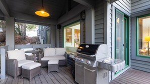 Een terras buiten met een barbecue, rieten meubilair en uitzicht op het huis.