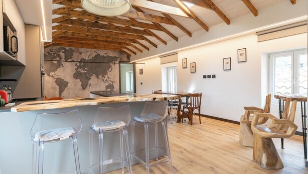 A spacious kitchen with a wooden ceiling, a world map wall, and a bar area with clear stools. - 4 Elements - Italian GuestHouse (Calolziocorte)