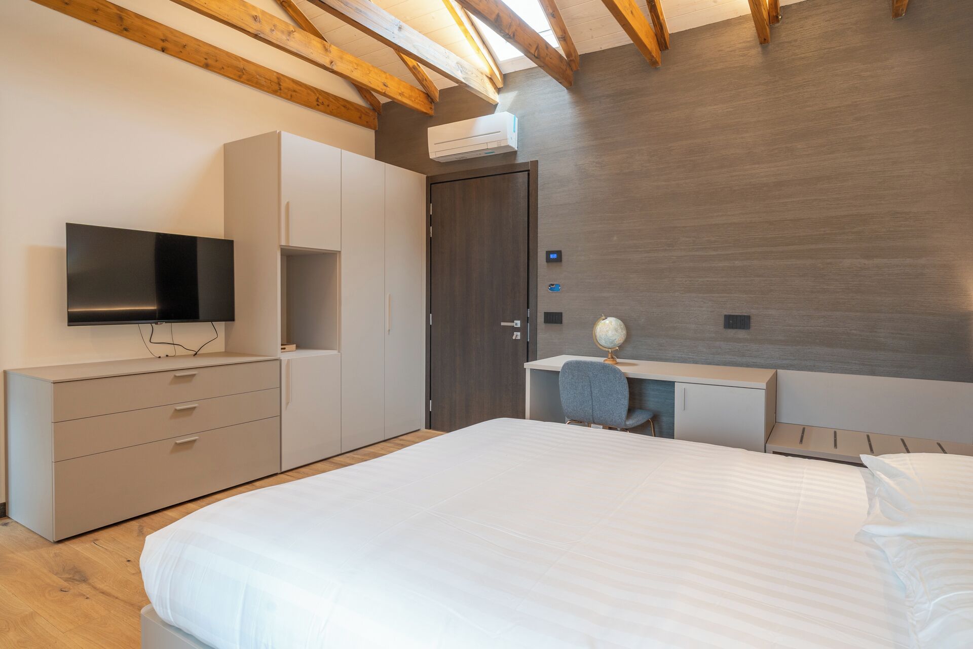 Een moderne slaapkamer met een groot bed, een televisie, een bureau met een wereldbol en een garderobe.
