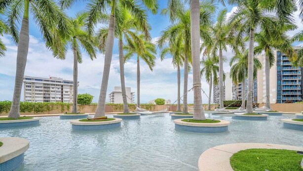 Zona de piscina con palmeras y un edificio al fondo.