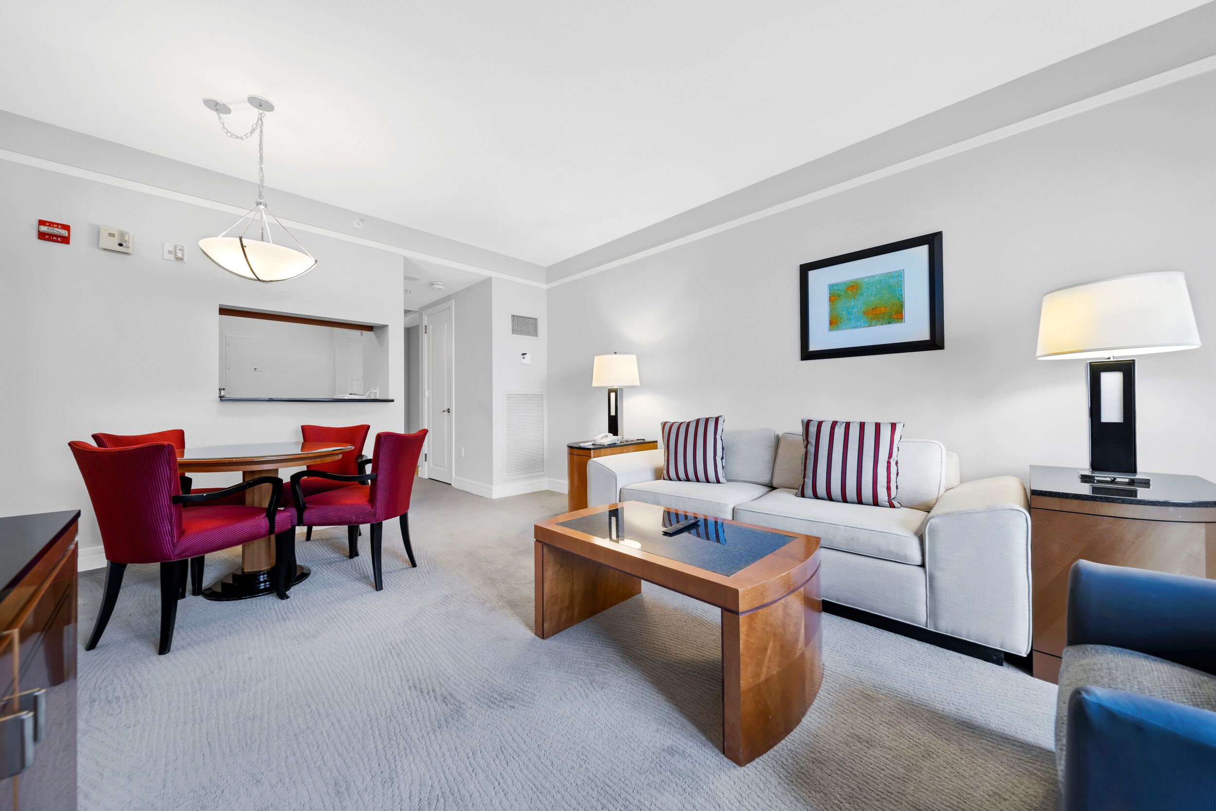 A modern hotel room with a dining area, a sofa set, a coffee table, and a lamp.