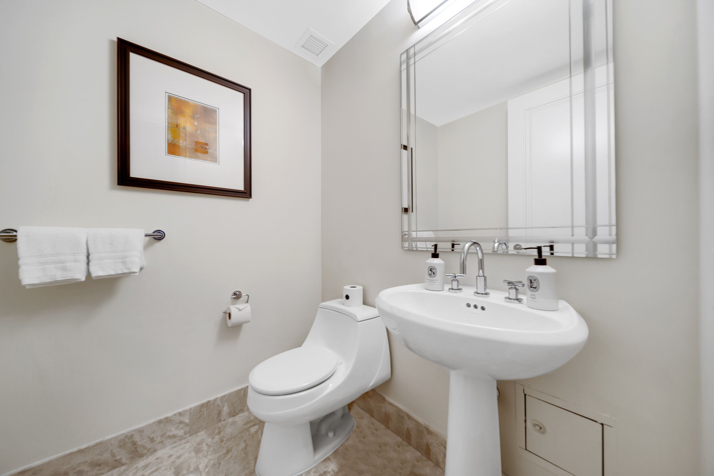 A modern bathroom with a toilet, sink, and framed artwork on the wall.