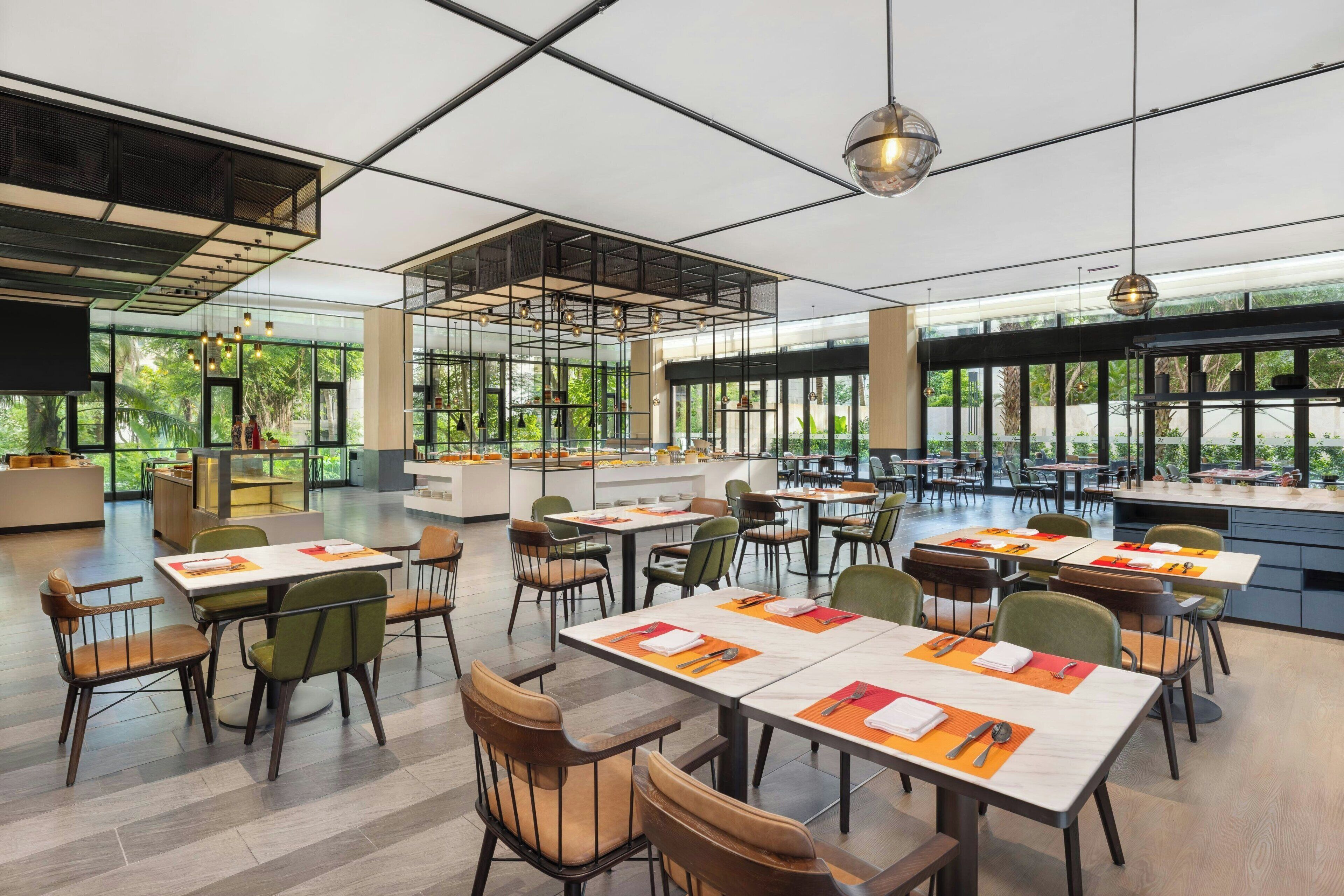 A spacious dining area with multiple tables and chairs, large windows, and a high ceiling with exposed beams.