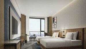 Habitació d'hotel moderna amb dos llits, una taula, una cadira i un gran finestral amb vista a la ciutat.