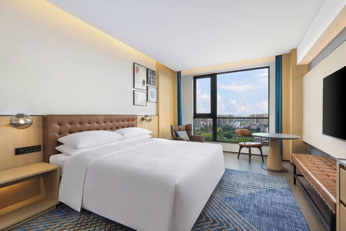 A hotel room with a large bed, a desk, a chair, a round table, and a TV.